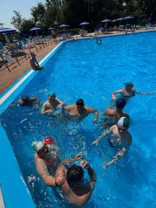 Un gruppo di ragazzi e ragazze in acqua nella parte bassa di una piscina all'aperto, con gli educatori accanto a loro