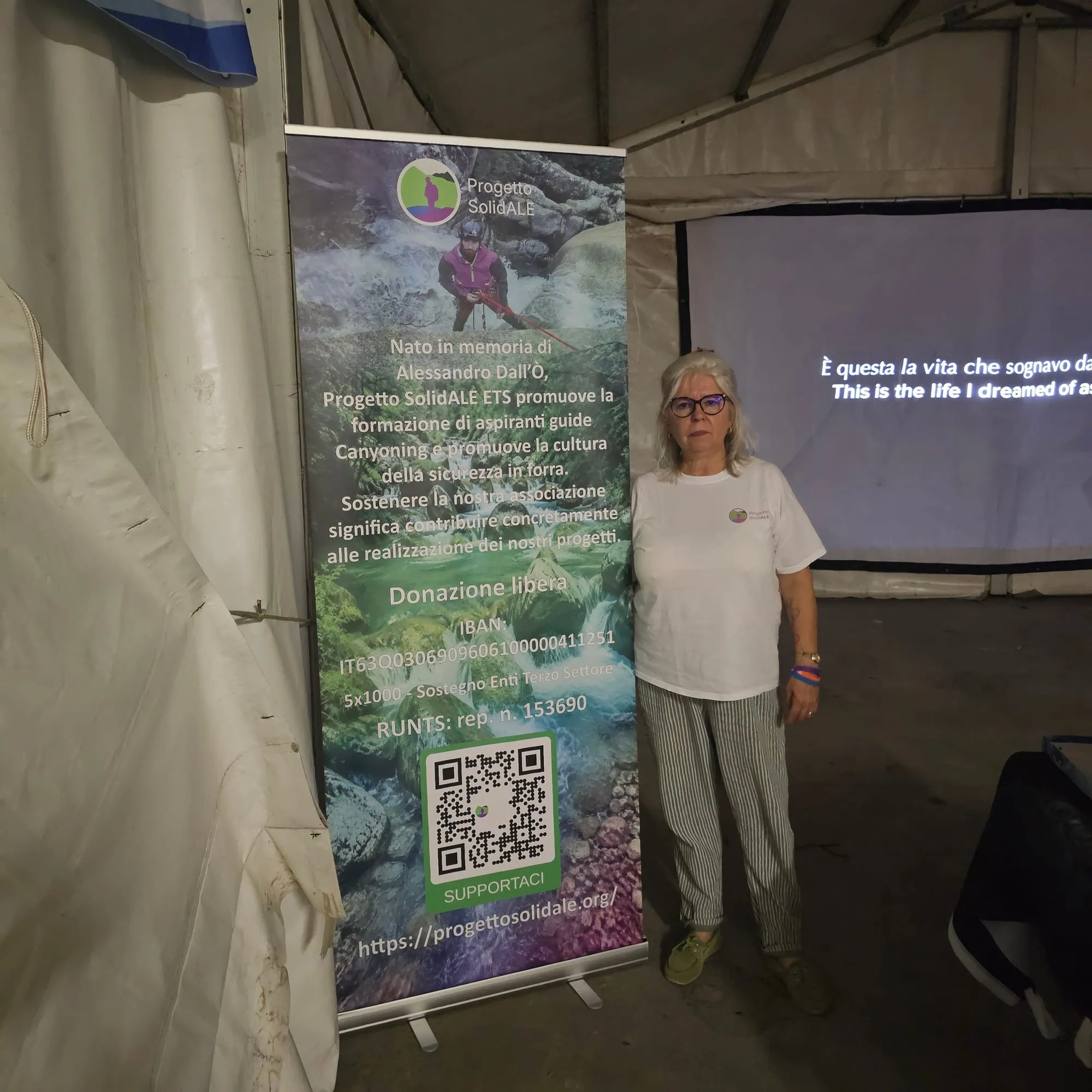 Una rappresentante del Comitato in piedi accanto al roll-up, con lo schermo acceso alle spalle