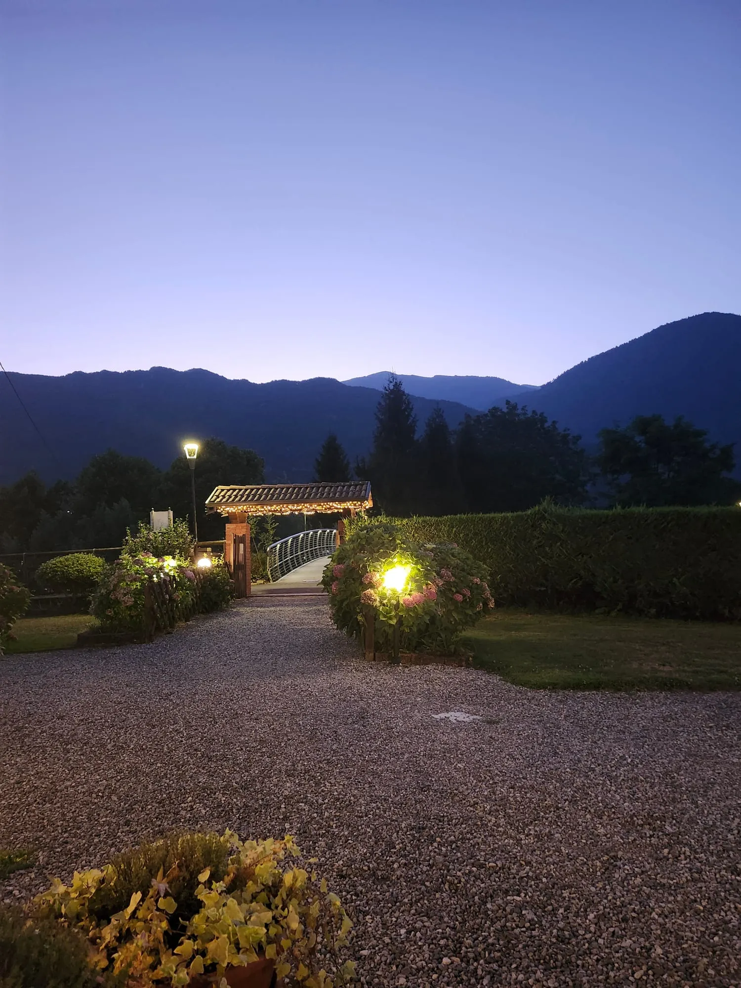 Un cancello illuminato in un giardino al crepuscolo, con le montagne della Val Sabbia sullo sfondo