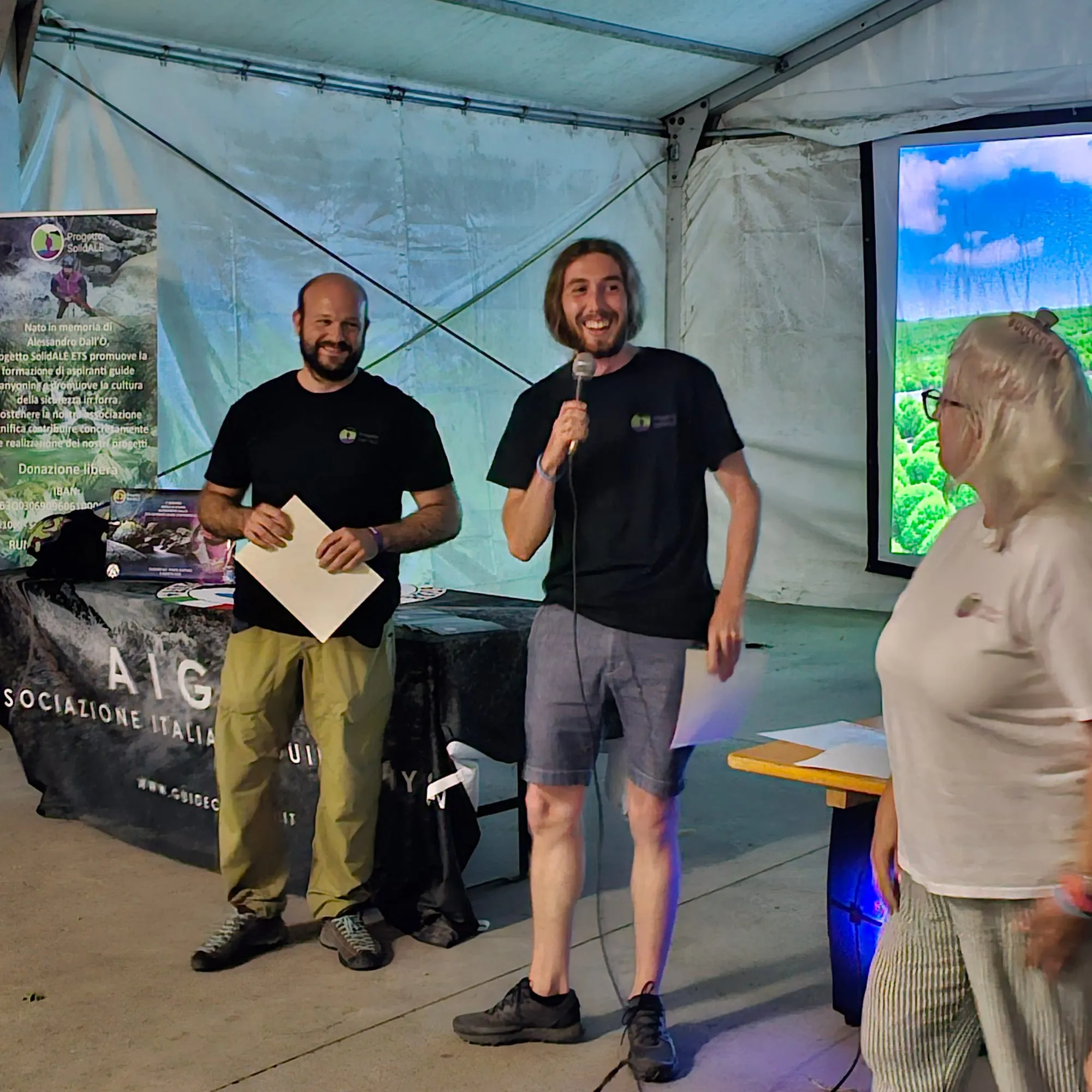 I due assegnatari della borsa di studio al microfono durante la serata del raduno, accanto al roll-up del Comitato Progetto SolidALE