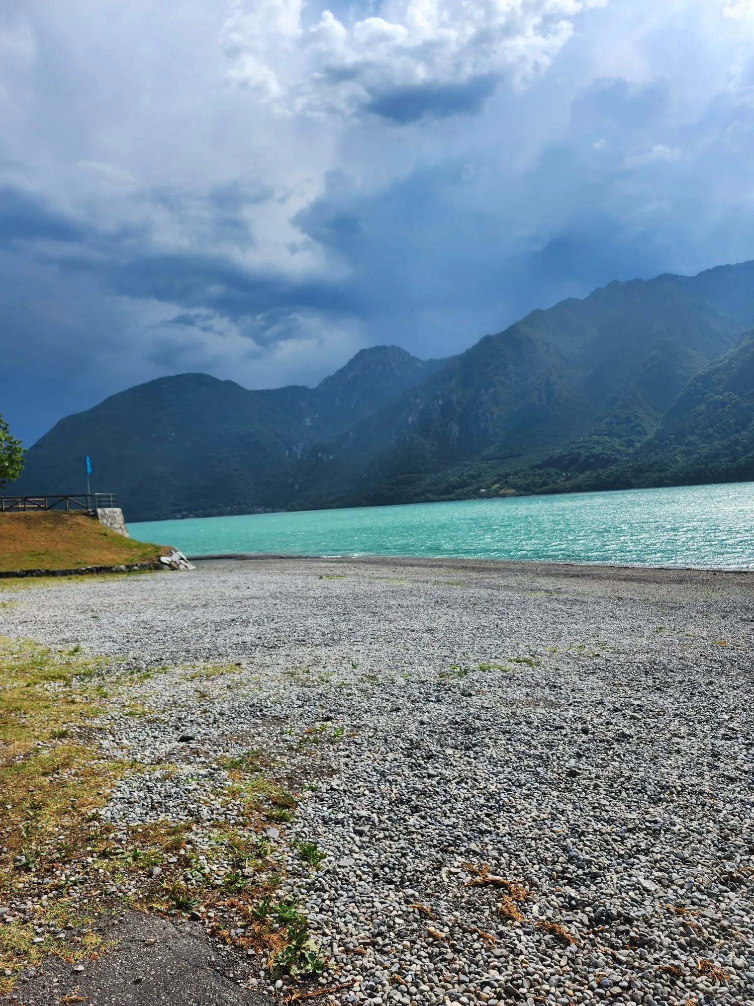 La spiaggia di ghiaia di Ponte Caffaro sul Lago d'Idro, con le montagne e un cielo carico di nuvole