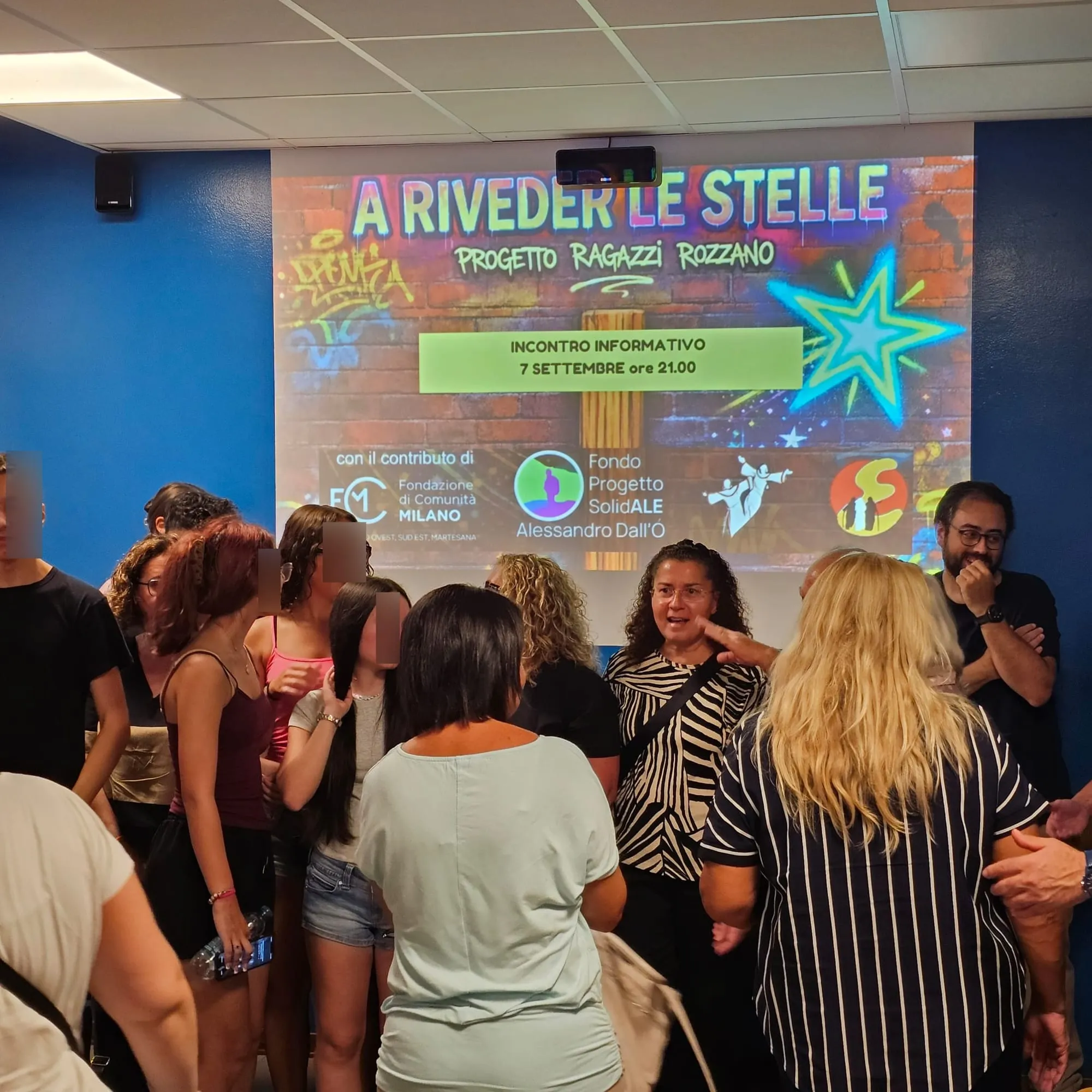 Ragazzi e adulti in piedi che parlano fra loro davanti allo schermo, al termine dell'incontro