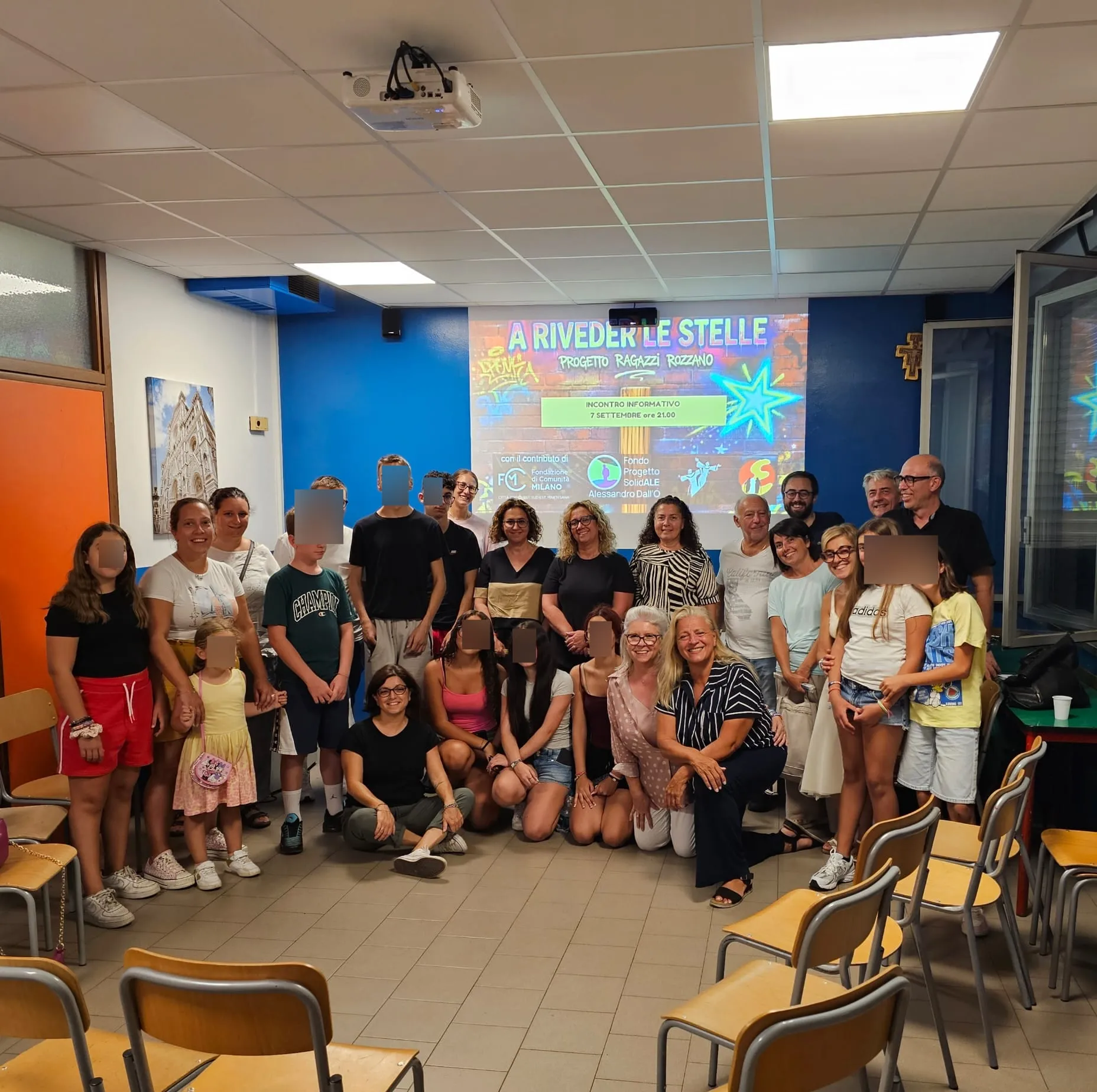 La foto di gruppo al termine dell'incontro informativo: ragazzi, famiglie ed educatori davanti allo schermo con il logo di «A riveder le stelle»